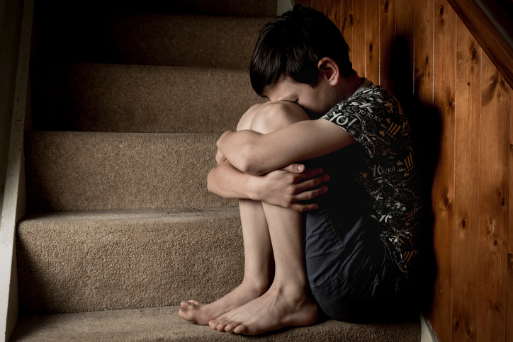 Sad, bullied or abused boy crying sitting on stairs