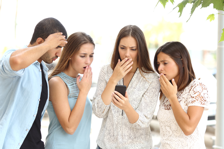 Four worried multi ethnic friends watching a smart phone in the street