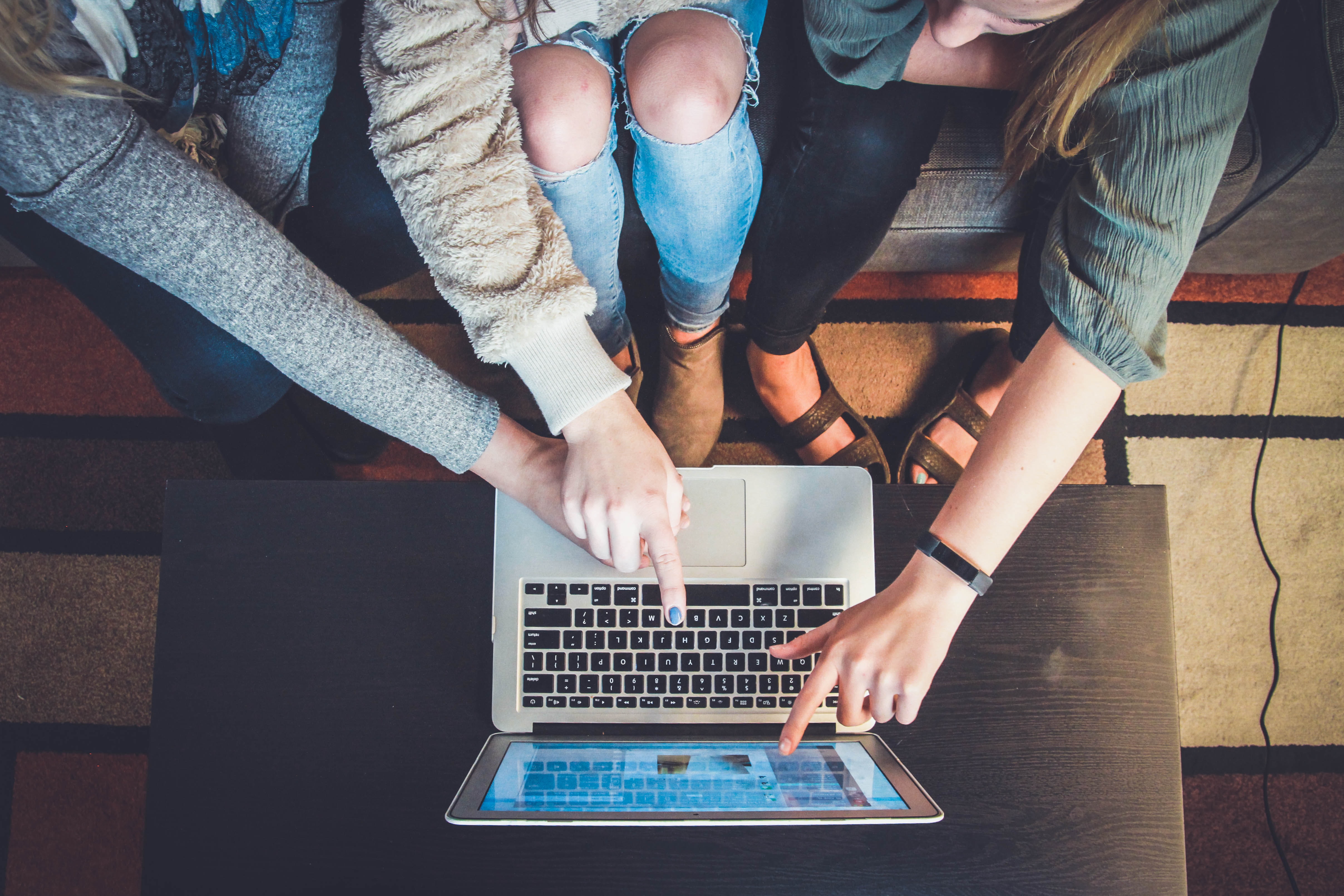 laptop sitting on table with 3 people in front of it pointing at the screen