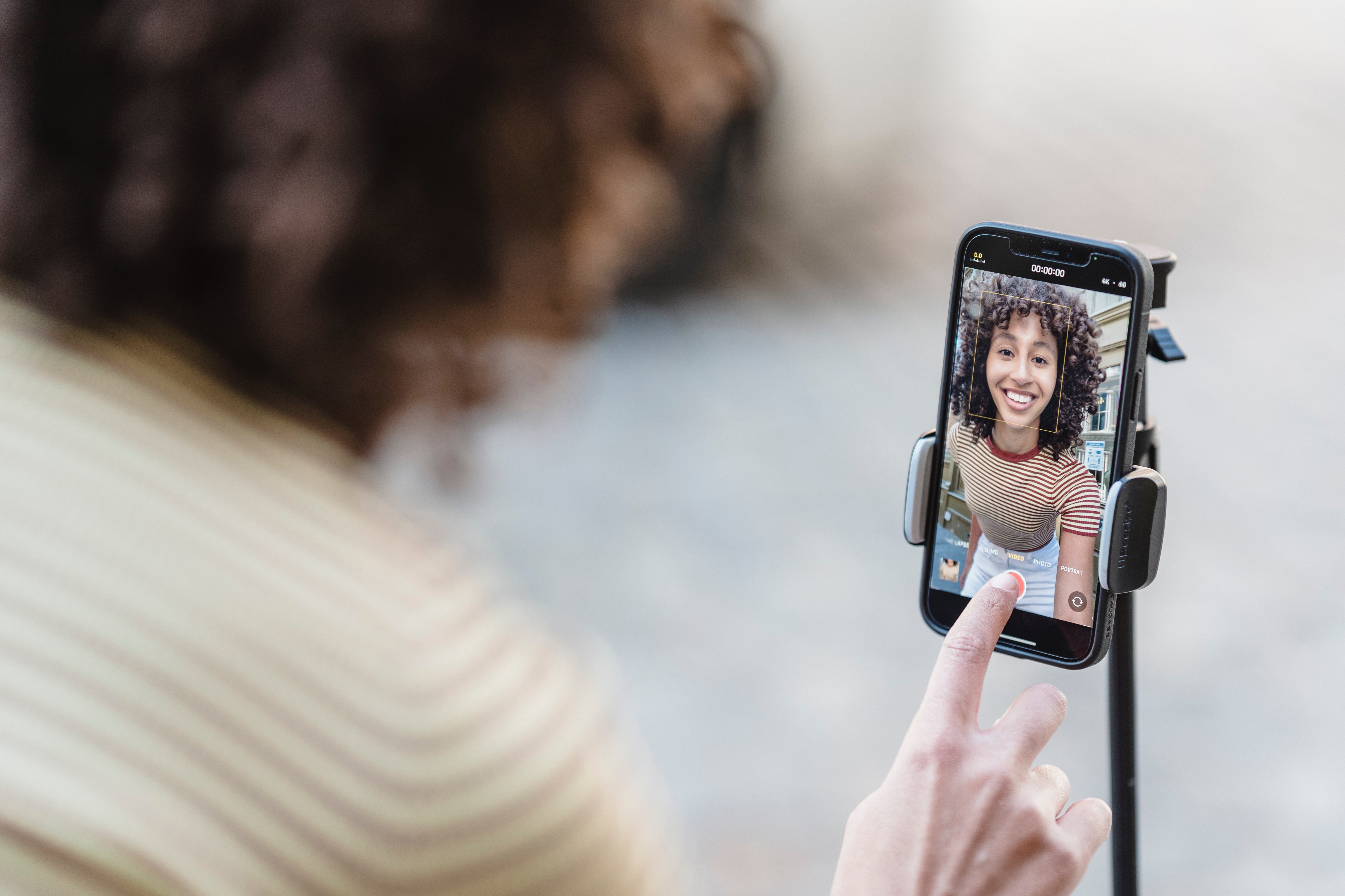 woman pressing the record button on a spartphone that is docked on a tripod